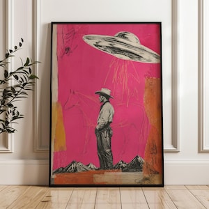 May include: A framed wall art print featuring a black and white illustration of a cowboy standing next to a horse against a vibrant magenta background. Above the cowboy, a large flying saucer descends with light beams, and dark mountains sit below.