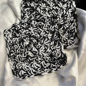 May include: Two black and white crocheted squares with a textured pattern. The squares are made with a thick yarn and have a slightly raised texture.