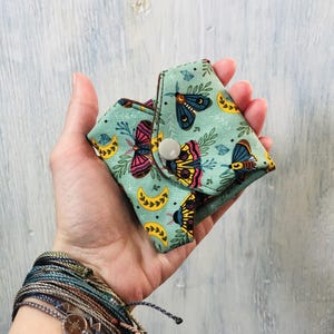 May include: A folded reusable menstrual pad with a green background and a colorful butterfly pattern. The pad has a snap closure.