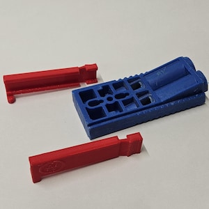 May include: A blue plastic jig with two red plastic guides. The jig has a grid pattern and is used for woodworking.
