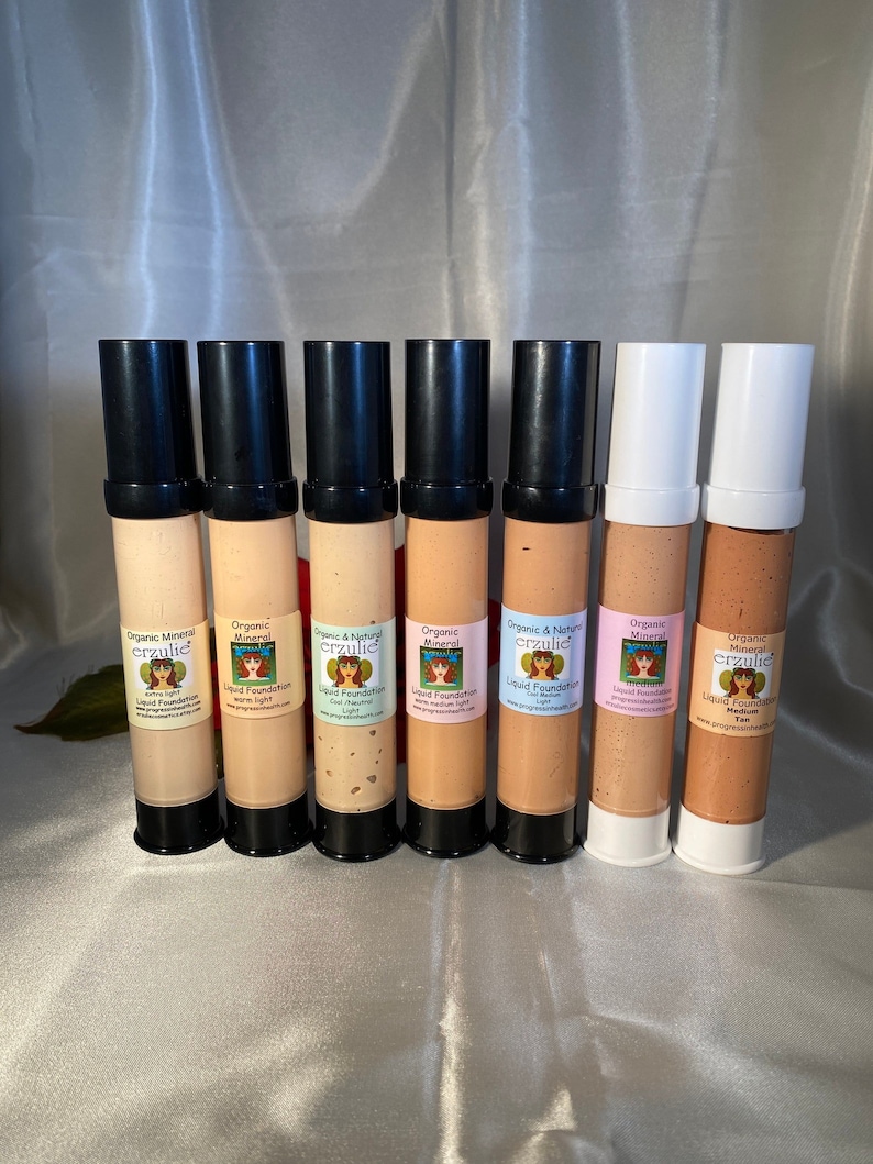 May include: Eight bottles of organic mineral makeup foundation in various shades. The bottles are labeled with the brand name "erzulie" and the words "Organic Mineral Makeup" and "Liquid Foundation".
