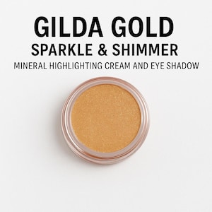 Pode incluir: Um recipiente circular de creme iluminador mineral e sombra para os olhos Gilda Gold. O produto tem uma cor dourada brilhante e está em um recipiente de plástico transparente. O texto "Gilda Gold Sparkle & Shimmer" está acima do produto.