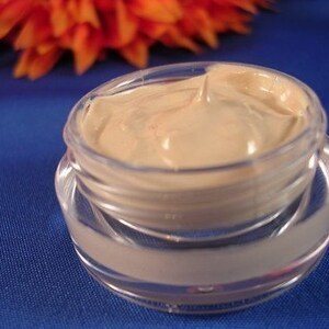 May include: A clear glass jar with a beige cream inside. The cream is thick and smooth, and it has a slight sheen.