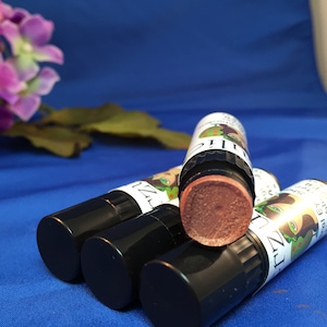May include: Four black and green lip balm tubes with a brown lip balm inside. The lip balm tubes have a label with a cartoon image of a woman with green hair and a green face.
