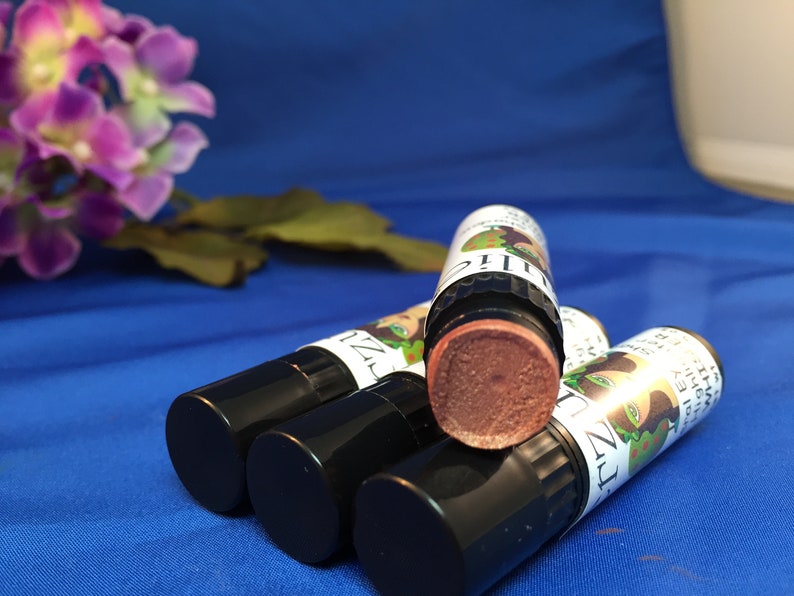 May include: Four black and green lip balm tubes with a brown lip balm inside. The lip balm tubes have a label with a cartoon image of a woman with green hair and a green face.