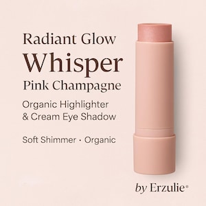 May include: A pink and white stick of organic highlighter and cream eye shadow called "Whisper Pink Champagne" by Erzulie. The product is described as having a soft shimmer.