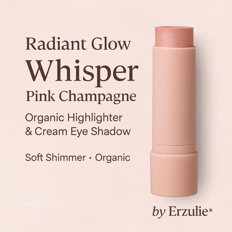 May include: A pink and white stick of organic highlighter and cream eye shadow called "Whisper Pink Champagne" by Erzulie. The product is described as having a soft shimmer.