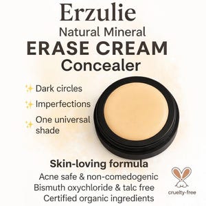 Puede incluir: Primer plano de un corrector beige en un recipiente negro. El texto dice "Erzulie ERASE CREAM Concealer" y destaca beneficios como cubrir ojeras e imperfecciones. El producto es libre de crueldad animal y está elaborado con ingredientes orgánicos.