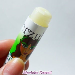 Op de afbeelding: Een witte lippenbalsem tube met een groen-wit label waarop een cartoon vrouw met groene ogen en een bloemenkrans te zien is. Het label heeft de tekst "Erzu" in zwarte letters.