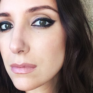 May include: Close-up of a woman's face with dark eyeliner and a neutral lip color. Her hair is dark and long.