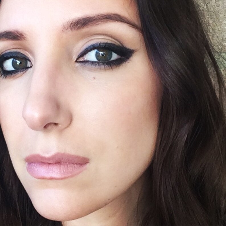 May include: Close-up of a woman's face with dark eyeliner and a neutral lip color. Her hair is dark and long.