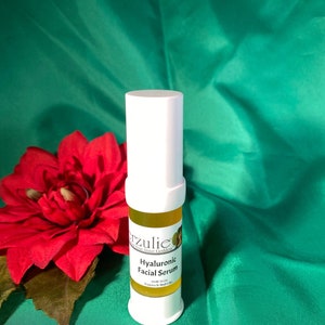 以下が含まれることがあります： 黄色い液体が詰まった小さな白いボトル。ボトルには「Hyaluronic Facial Serum」と「Erzulie - Awaken Your Inner Goddess」のラベルが貼られています。