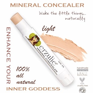Puede incluir: Un corrector mineral blanco con la marca "Erzulie" y la palabra "light". El producto está etiquetado como 100% natural y libre de crueldad. La imagen también incluye el texto "Enhance Your Inner Goddess".