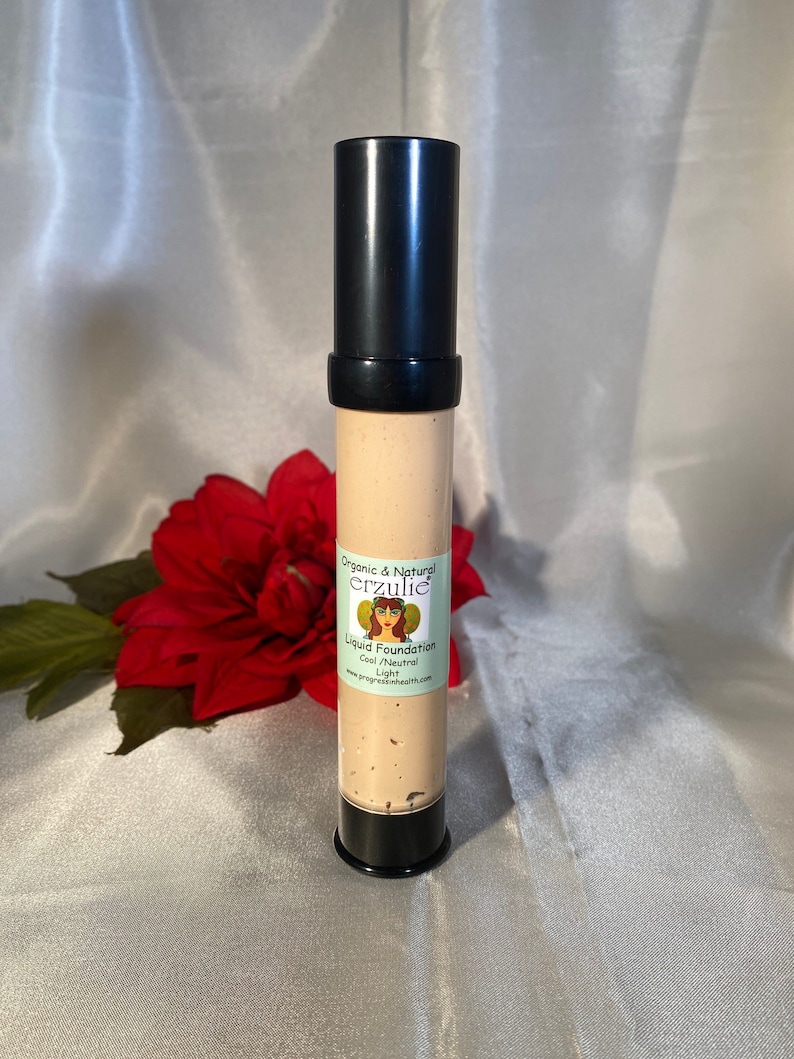 May include: A tube of organic and natural liquid foundation in the shade Cool Neutral Light by the brand Erzulie. The tube is black with a white label and features a drawing of a woman with wings.