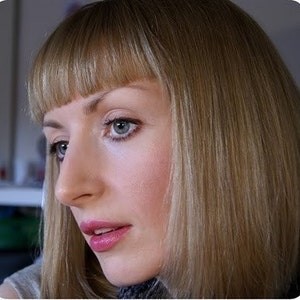 Puede incluir: Retrato en primer plano de una persona con piel clara, cabello rubio claro y ojos azules. La persona mira ligeramente hacia la izquierda, con una expresi&oacute;n neutra. El cabello est&aacute; peinado con flequillo. Los labios est&aacute;n pintados con un l&aacute;piz labial rosa.