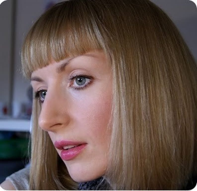 Puede incluir: Retrato en primer plano de una persona con piel clara, cabello rubio claro y ojos azules. La persona mira ligeramente hacia la izquierda, con una expresi&oacute;n neutra. El cabello est&aacute; peinado con flequillo. Los labios est&aacute;n pintados con un l&aacute;piz labial rosa.