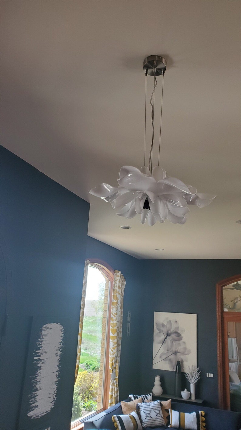 Może przedstawiać: Biała, kwiatowa lampa wisząca zwisająca z sufitu w pokoju z niebieskimi ścianami, oknem z ż&oacute;łtymi zasłonami i sofą z poduszkami.