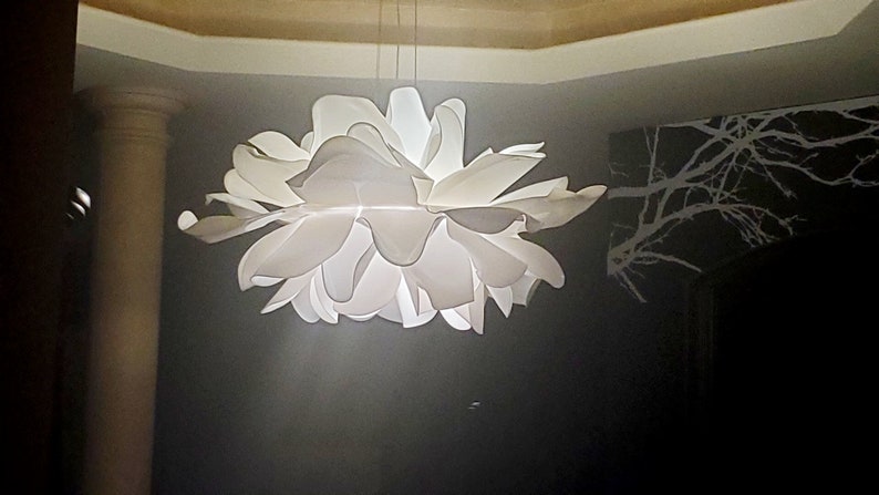 Może przedstawiać: Biała, papierowa lampa w kształcie kwiatu z wieloma warstwami płatk&oacute;w. Lampa jest zawieszona na suficie i jest oświetlona, dając miękkie światło.