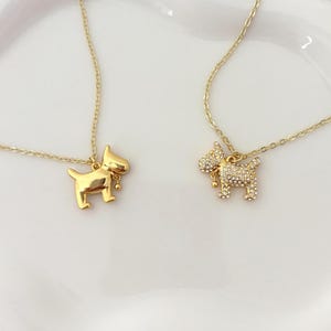 May include: Two gold-toned necklaces featuring dog-shaped pendants. One pendant has a smooth, polished gold finish, while the other is encrusted with small, clear sparkling crystals. Both pendants include a tiny dangling bell charm on a gold chain.
