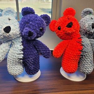 May include: Four handmade crochet teddy bears. Two are split down the middle with different colours. One is light blue and purple, the other is red and grey. The other two are light blue and grey. Each bear has black eyes and nose.