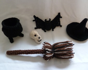 Op de afbeelding: Een set gehaakte Halloween-decoraties, waaronder een zwarte ketel, een zwarte heksenhoed, een bruin-witte bezem, een zwarte vleermuis en een witte schedel.
