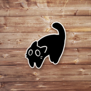 Pu&ograve; includere: Un adesivo di gatto nero con occhi grandi, che guarda a sinistra, con la coda arrotolata. L'adesivo &egrave; su uno sfondo di legno.