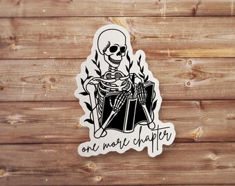 May include: A black and white sticker featuring a skeleton reading a book with the text "one more chapter" below. The skeleton is surrounded by leaves.