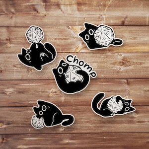 May include: Five black cat stickers with the word "Chomp" and a black and white dice with numbers 1, 2, 4, 6, 8, and 16.