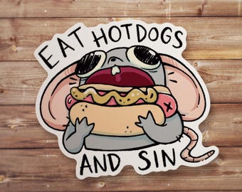 May include: A die-cut sticker featuring a cartoon gray mouse with large ears and wide eyes, holding a hot dog with mustard. The text EAT HOT DOGS AND SIN is printed in black capital letters above and below the illustration of the mouse.