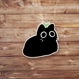 Pu&ograve; includere: Un adesivo di gatto nero con un piccolo germoglio verde sulla testa. Il gatto ha occhi grandi e un corpo rotondo.