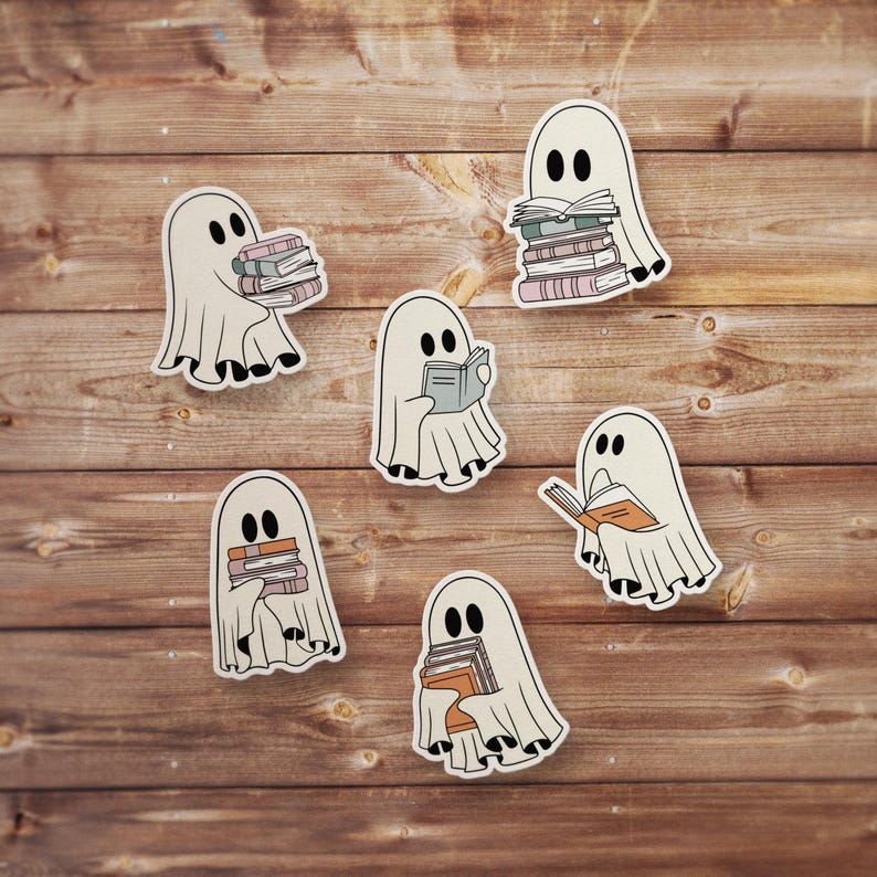 May include: Six white ghost stickers with black eyes and mouths, each holding a stack of books or a single book. The ghosts are on a wood background.
