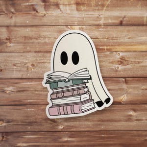 May include: A white ghost with a stack of books in front of it. The books are various shades of pink, green, and brown. The ghost is smiling and has two black eyes.