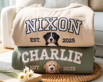 May include: Two sweatshirts, one tan and one olive green, are stacked. The tan sweatshirt says "NIXON" in white block letters with a black outline, a dog graphic, and "EST. 2025". The green sweatshirt says "CHARLIE" with a dog graphic and "EST. 2025".