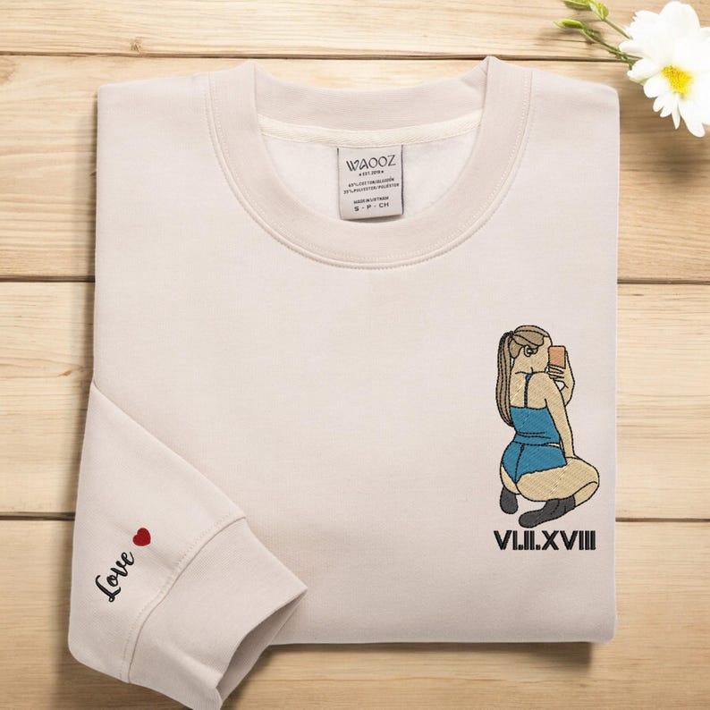 Może przedstawiać: Beżowa bluza z nadrukiem kobiety robiącej sobie selfie. Pod nadrukiem wyszyty jest tekst "VIII.II.XVIII". Na lewym rękawie wyszyty jest napis "Love" z czerwonym sercem.