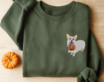 May include: A dark olive green crewneck sweatshirt featuring an embroidered graphic of a white dog wearing a ghost costume and holding an orange jack-o'-lantern bucket filled with colorful candies on the right side of the chest.