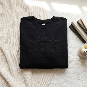 May include: A black crewneck sweatshirt featuring the embroidered text CT TECH in a collegiate font, positioned below a small row of five embroidered flying bats. The embroidery is executed in a matching black thread on the black fabric.