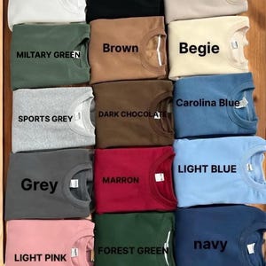 May include: A collection of 16 folded sweatshirts in various colors, including white, black, sand, brown, military green, beige, Carolina blue, sports grey, dark chocolate, light blue, grey, maroon, forest green, navy, and light pink.