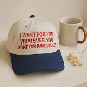 May include: A cream-colored baseball cap with a dark blue brim and a dark blue button on top. The front of the cap features red embroidered text that reads: I WANT FOR YOU WHATEVER YOU WANT FOR IMMIGRANTS. The cap has a structured six-panel design.