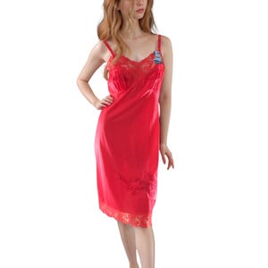 May include: A red slip dress with spaghetti straps and a lace-trimmed neckline and hem. The dress features a floral embroidery design near the hem and a small blue and white embellishment on the strap.