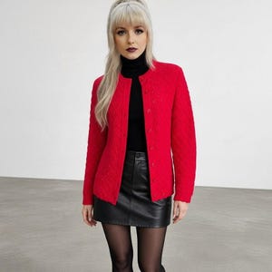 May include: A bright red long-sleeved cardigan with a textured diamond pattern and a row of matching buttons down the front. The cardigan is worn over a black turtleneck top and paired with a black leather mini skirt and sheer black tights.