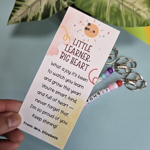 Puede incluir: Un marcap&aacute;ginas con el texto "Little Learner, Big Heart" y un mensaje de la Sra. Elizabeth, junto con dos llaveros. Los llaveros tienen cuentas de colores y el nombre "Joshua".
