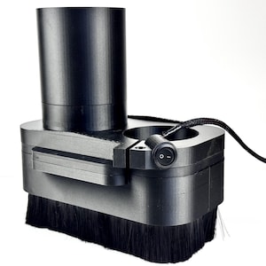 May include: A black CNC router dust shoe with a cylindrical top, a brush base, and an integrated on/off switch. The device has a circular design with a black power cord.