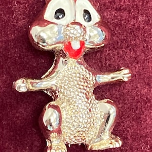 May include: A silver-colored cartoon squirrel pin with red painted details. The squirrel is sitting up with its arms outstretched and has a wide smile.