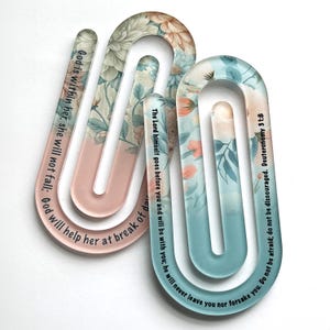Peut inclure: Deux marque-pages en forme de U avec des motifs floraux et des citations inspirantes. L'un est rose avec un motif floral et le texte "Dieu est en elle, elle ne tombera pas." L'autre est bleu avec un texte de Deutéronome 31:8.