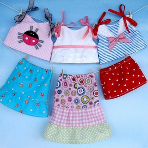 May include: Five doll clothes hanging on a clothesline. The clothes are a pink top with a ladybug, a white top with lace, a blue and white striped top, a blue skirt with white flowers, and a multi-colored skirt with pink, green, and white.