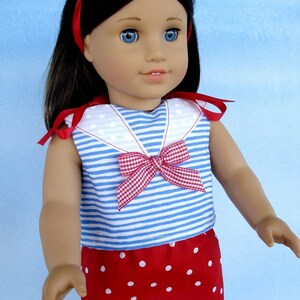 May include: A doll wearing a blue and white striped sailor top with a red and white gingham bow and a red skirt with white polka dots. The doll has long dark hair and blue eyes.