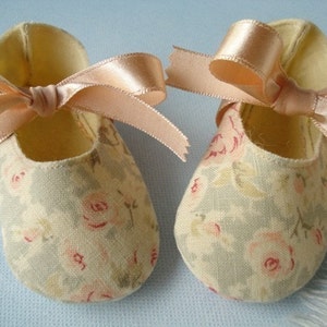 May include: A pair of baby shoes with a floral print and a satin ribbon tied in a bow. The shoes are light blue and cream with a pink floral pattern.