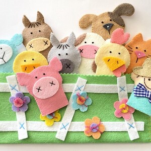 May include: A set of felt finger puppets featuring farm animals, including a pig, cow, chicken, sheep, horse, dog, and a farmer. The puppets are arranged in a green felt pouch with white stitching and blue cross-stitches.