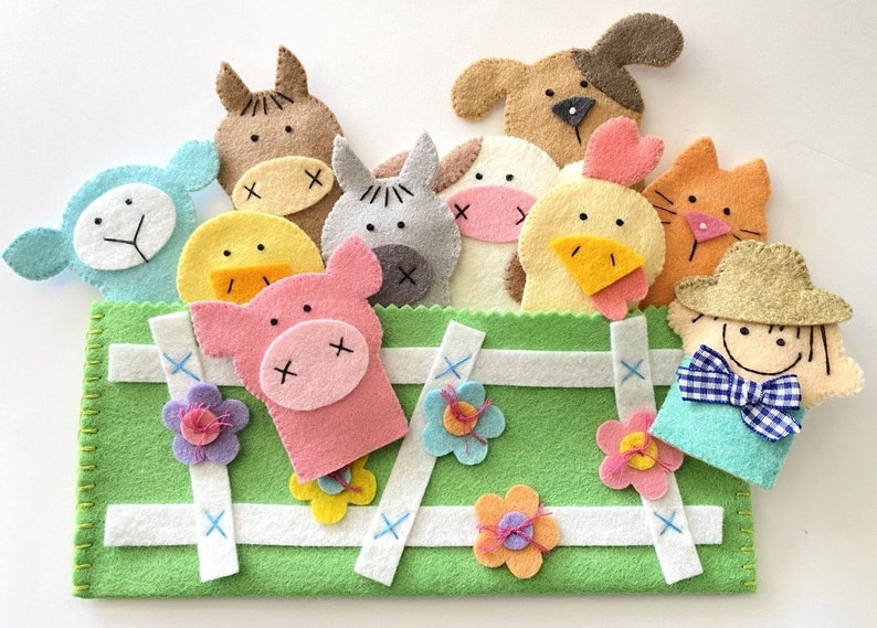 May include: A set of felt finger puppets featuring farm animals, including a pig, cow, chicken, sheep, horse, dog, and a farmer. The puppets are arranged in a green felt pouch with white stitching and blue cross-stitches.