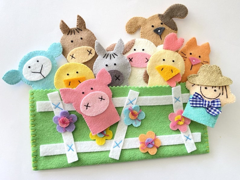 May include: A green felt puppet theater with a white picket fence design. The theater includes felt finger puppets of a pig, a cow, a chicken, a sheep, a horse, a cat, a dog, and a farmer.